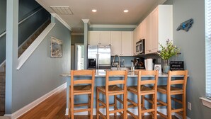 A modern kitchen with a central island, white cabinets, stainless steel appliances, and a wooden dining area. - Enjoy Belle of the Beach -  Your Family Get Away!  **Linens Included** (Carolina Beach)