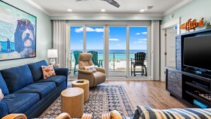 A living room with a blue sofa, a coffee table, a TV, and a ceiling fan. - Sterling Sands 313 - On the Beach! Renovated 2B/2B w/Pool/Hot Tub/Garage Parking (Destin)