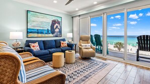 A living room with a large painting, a ceiling fan, a sofa, a chair, and a view of the beach. - Sterling Sands 313 - On the Beach! Renovated 2B/2B w/Pool/Hot Tub/Garage Parking (Destin)