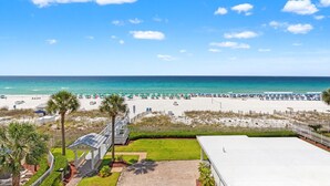 A beach view with a white building, palm trees, and a clear sky. - Sterling Sands 313 - On the Beach! Renovated 2B/2B w/Pool/Hot Tub/Garage Parking (Destin)