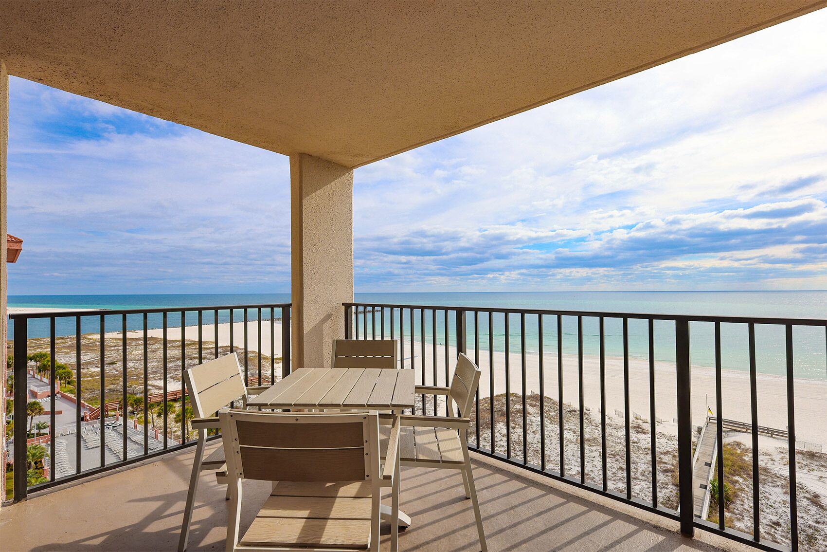 A balcony with a table and chairs, overlooking a beach with a clear sky.