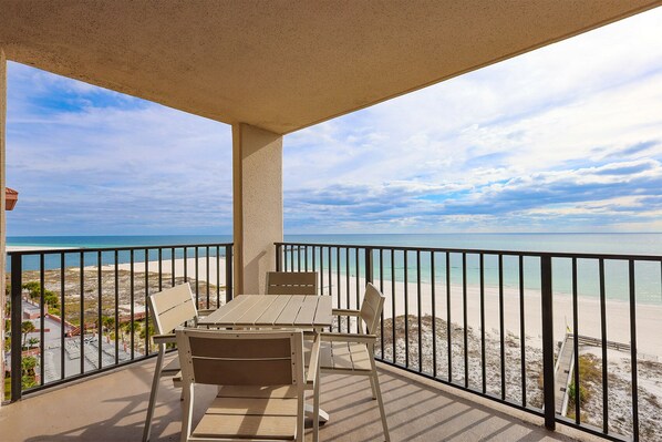 Een balkon met een tafel en stoelen, met uitzicht op een strand en een heldere lucht.