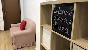 A room with a wooden cabinet, a red cushion on a checkered sofa, and a chalkboard with "Welcome to Casa Flor" written on it. - CasaCondo @Flora: Relax in a Spacious Condo with Jacuzzi - Your Naples Getaway (Torre del Greco)