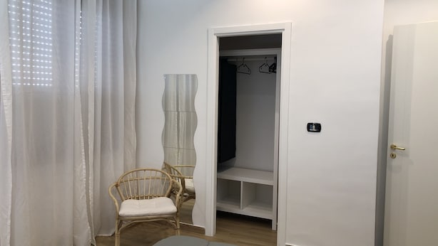 A room with a bed, a chair, a wardrobe, and a hanging rack. - CasaCondo @Flora: Relax in a Spacious Condo with Jacuzzi - Your Naples Getaway (Torre del Greco)
