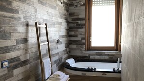 A bathroom with a wooden floor, a white toilet, a wooden chair with towels, a bathtub, and a window with blinds. - CasaCondo @Flora: Relax in a Spacious Condo with Jacuzzi - Your Naples Getaway (Torre del Greco)