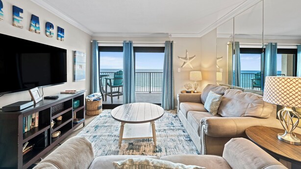 A living room with a TV, sofa, coffee table, and a view of the sea.