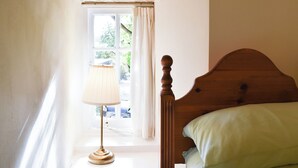A bedroom with a wooden headboard, a bedside lamp, a window with curtains, and a view of greenery outside. - 2 bedroom accommodation in Yougrave, near Bakewell (Yougrave, near Bakewell)
