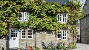 A stone building with a white door, multiple windows, and a small outdoor seating area with chairs and a table. - 2 bedroom accommodation in Yougrave, near Bakewell (Yougrave, near Bakewell)