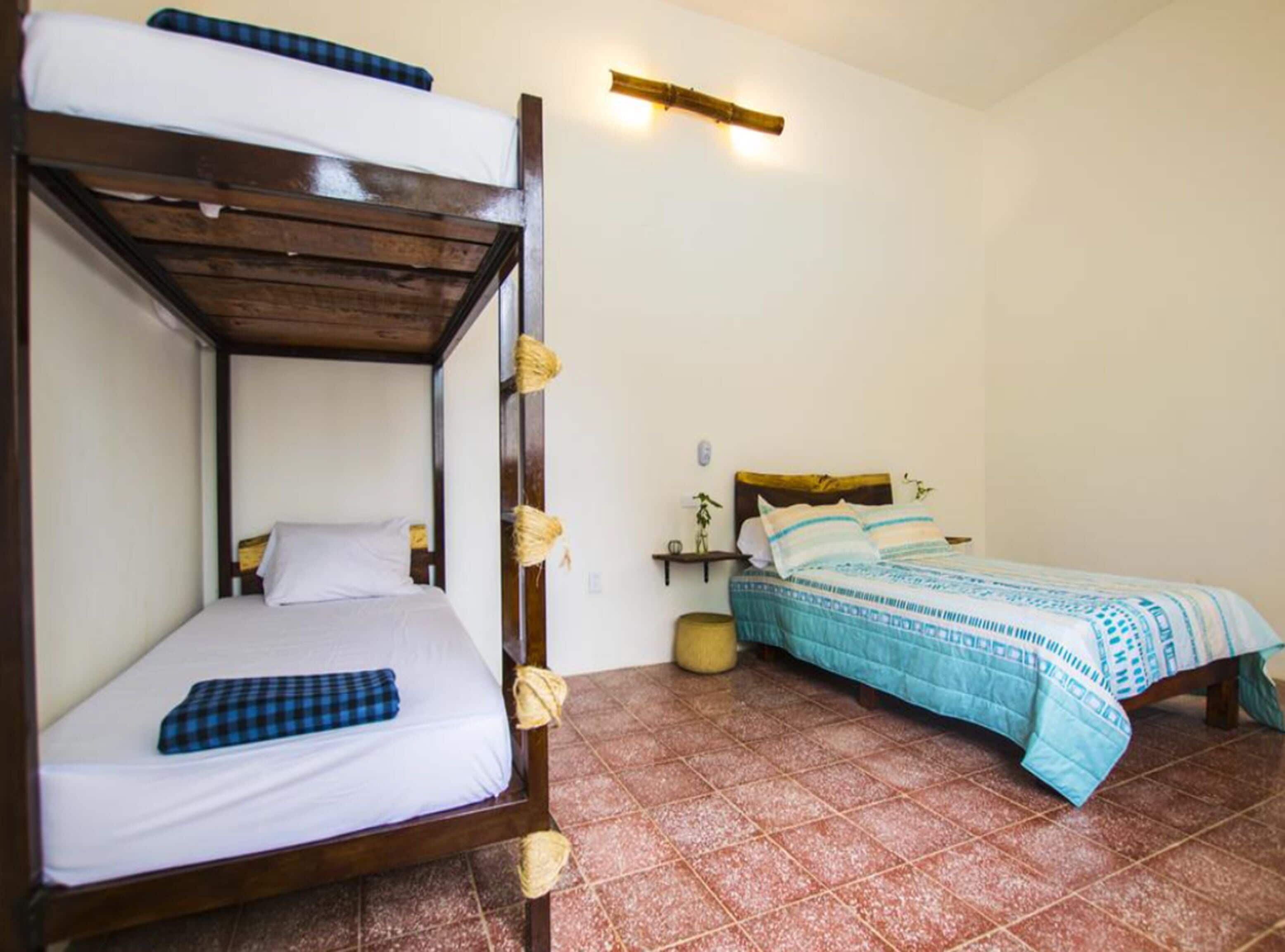 Una habitación con una cama litera y una cama individual, ambas con ropa de cama blanca y detalles en azul.