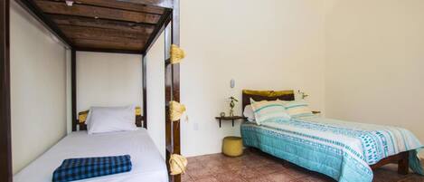 Una habitación con una cama litera y una cama individual, ambas con ropa de cama blanca y detalles en azul.