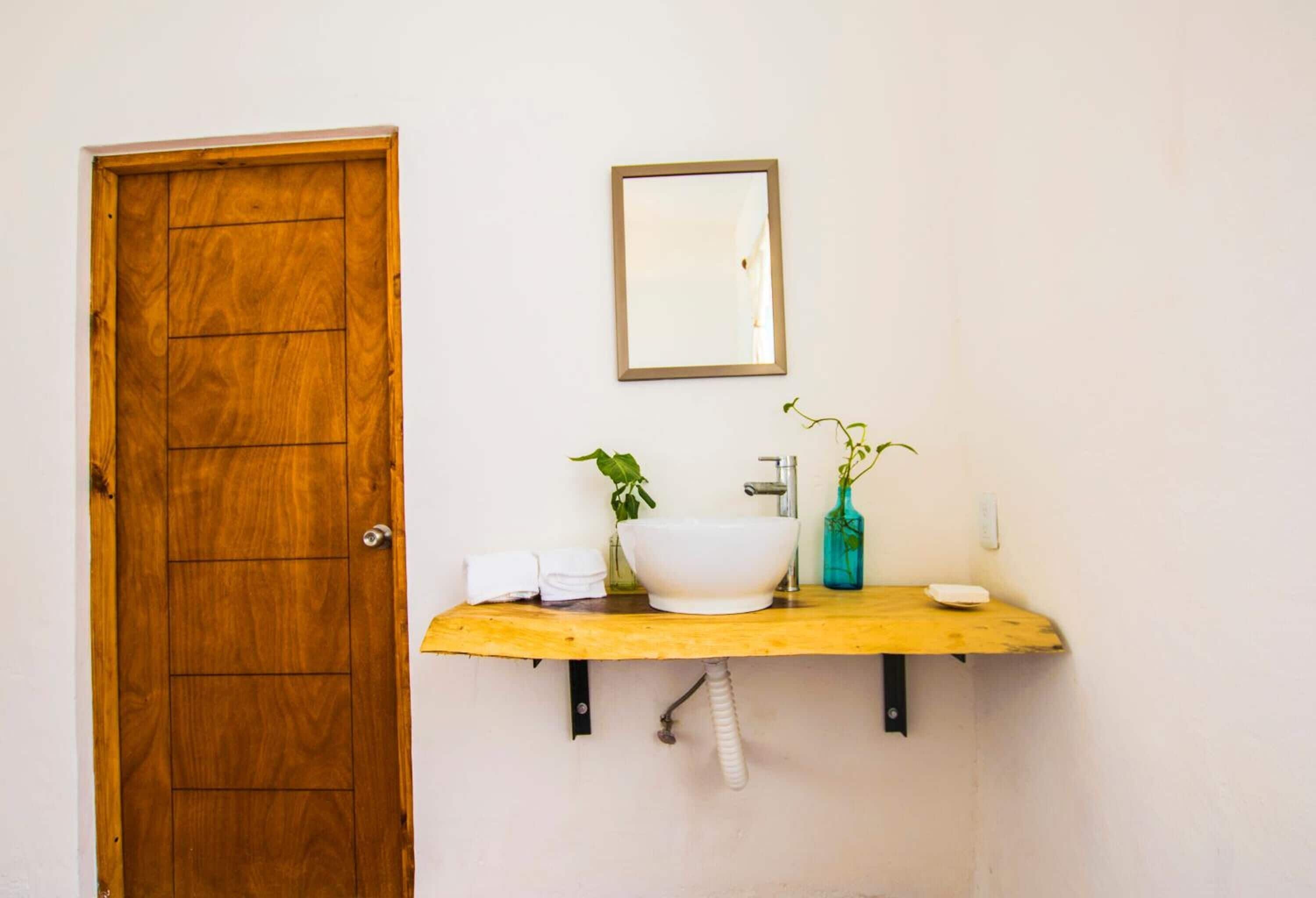 A bathroom with a wooden door, a white sink, a mirror, and a small shelf with towels and a vase.