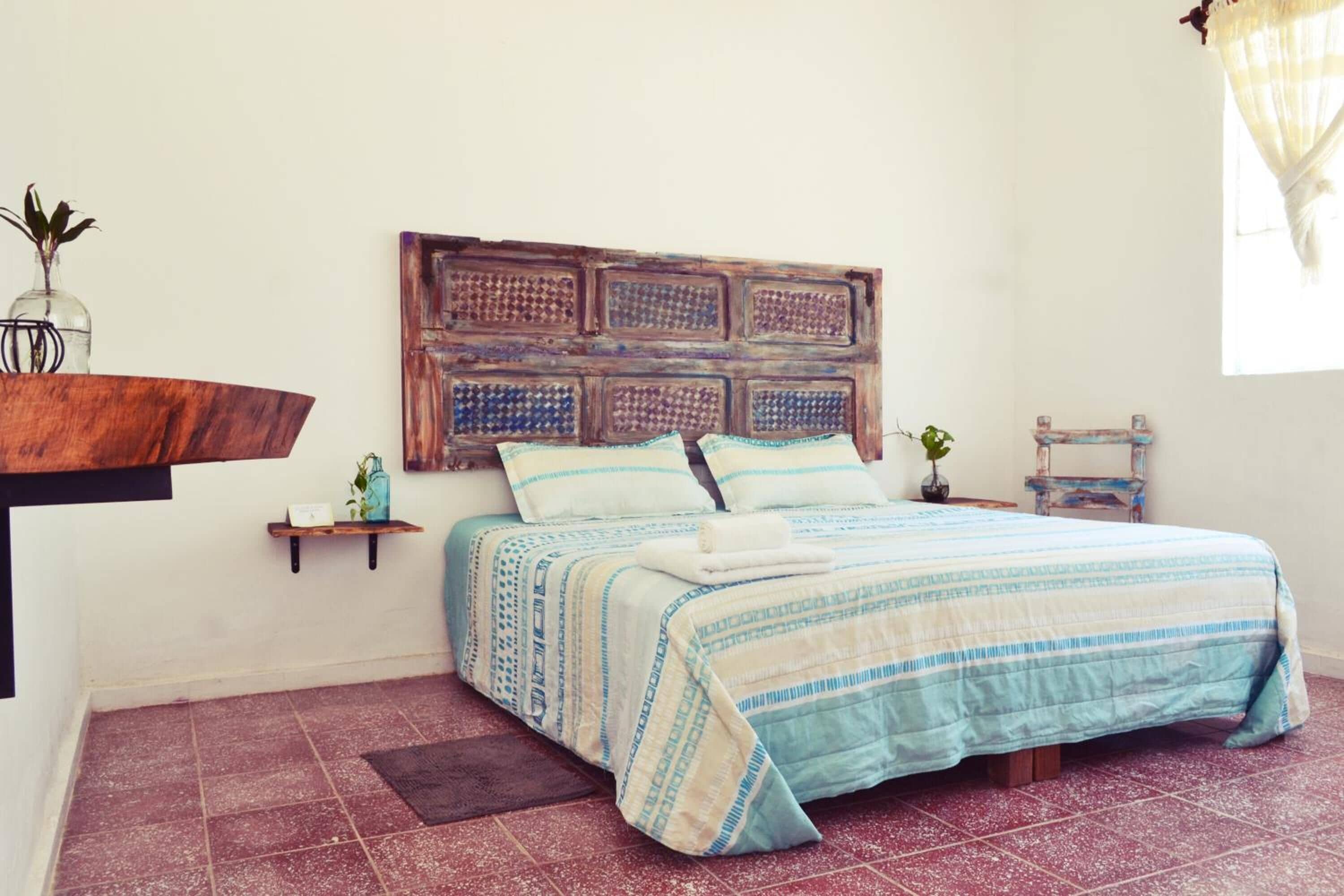 Un dormitorio con una cama, cabecera, estante con planta y una mesita con planta.