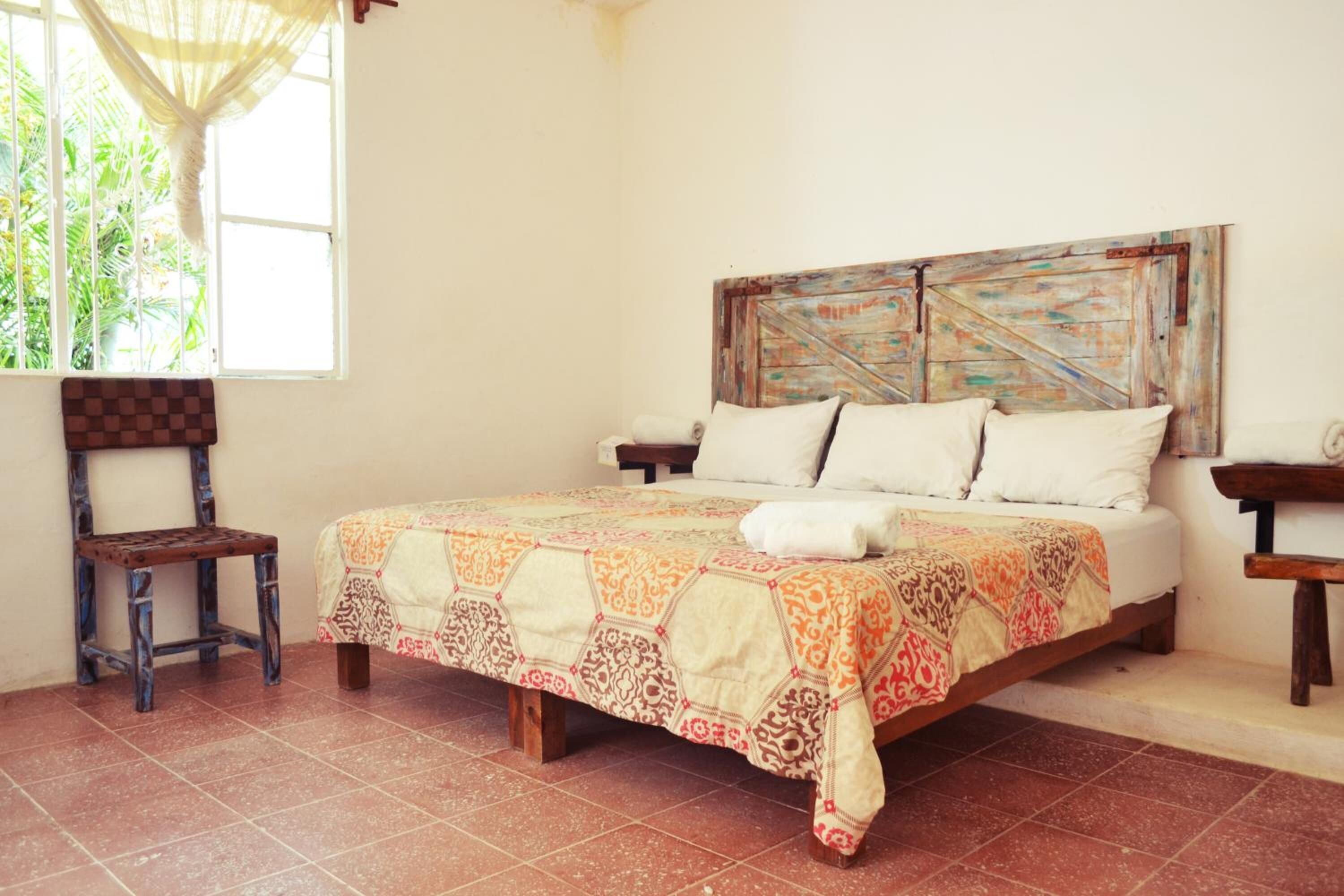 A bed with a patterned bedspread, a wooden headboard, and a window with a view of greenery.