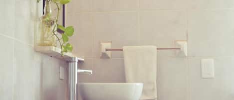 Un baño con un lavamanos blanco, un espejo y una planta en un florero de vidrio.