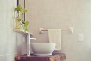 Un baño con un lavamanos blanco, un espejo y una planta en un florero de vidrio.