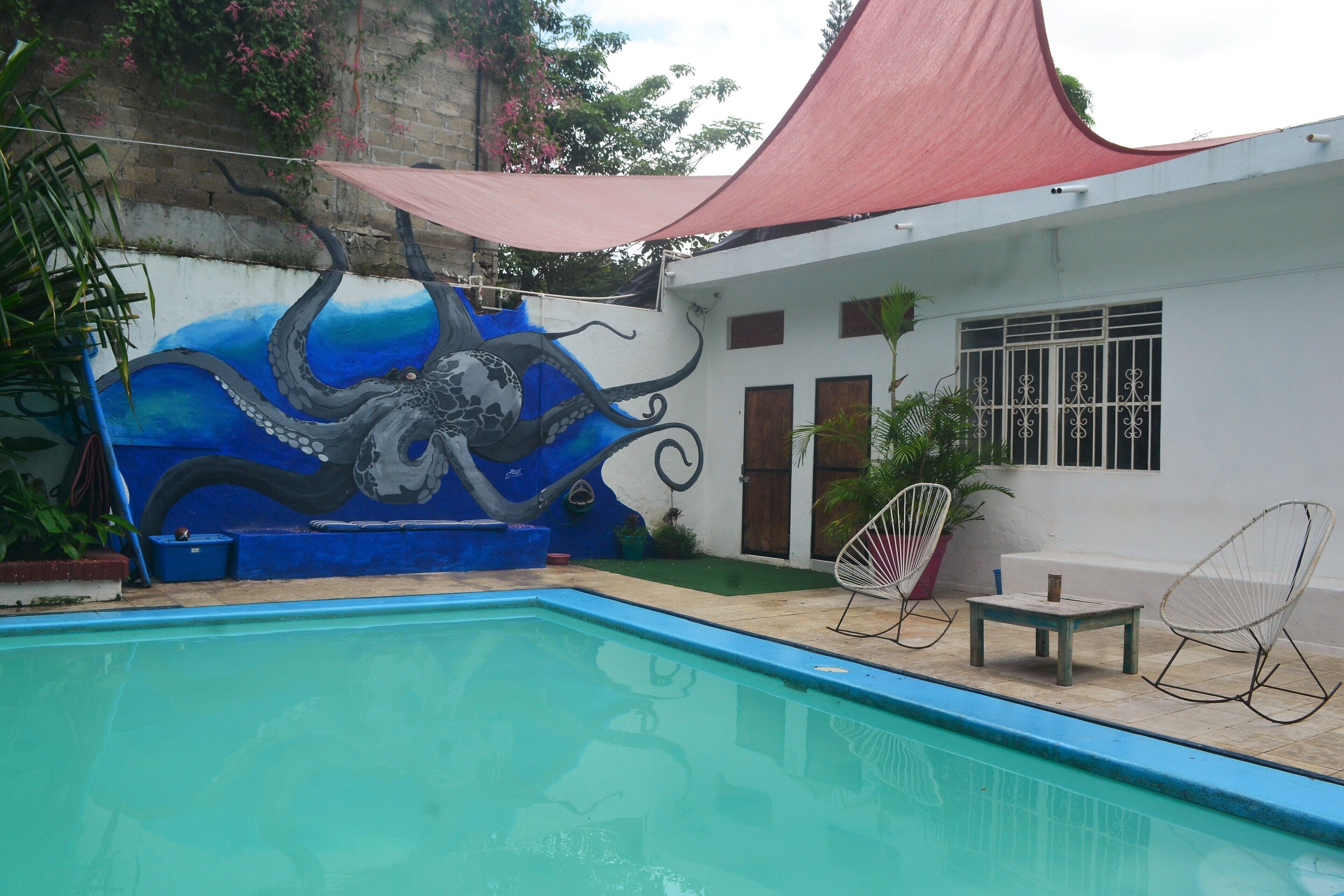A swimming pool with a mural of an octopus, a red canopy, and two chairs.