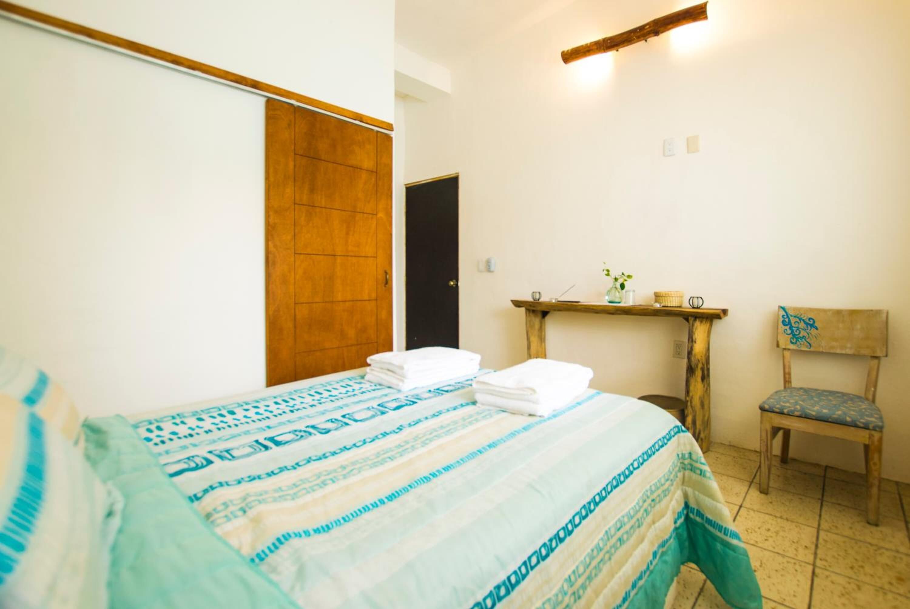 Un dormitorio con cama, armario de madera, silla y estante con artículos de aseo.