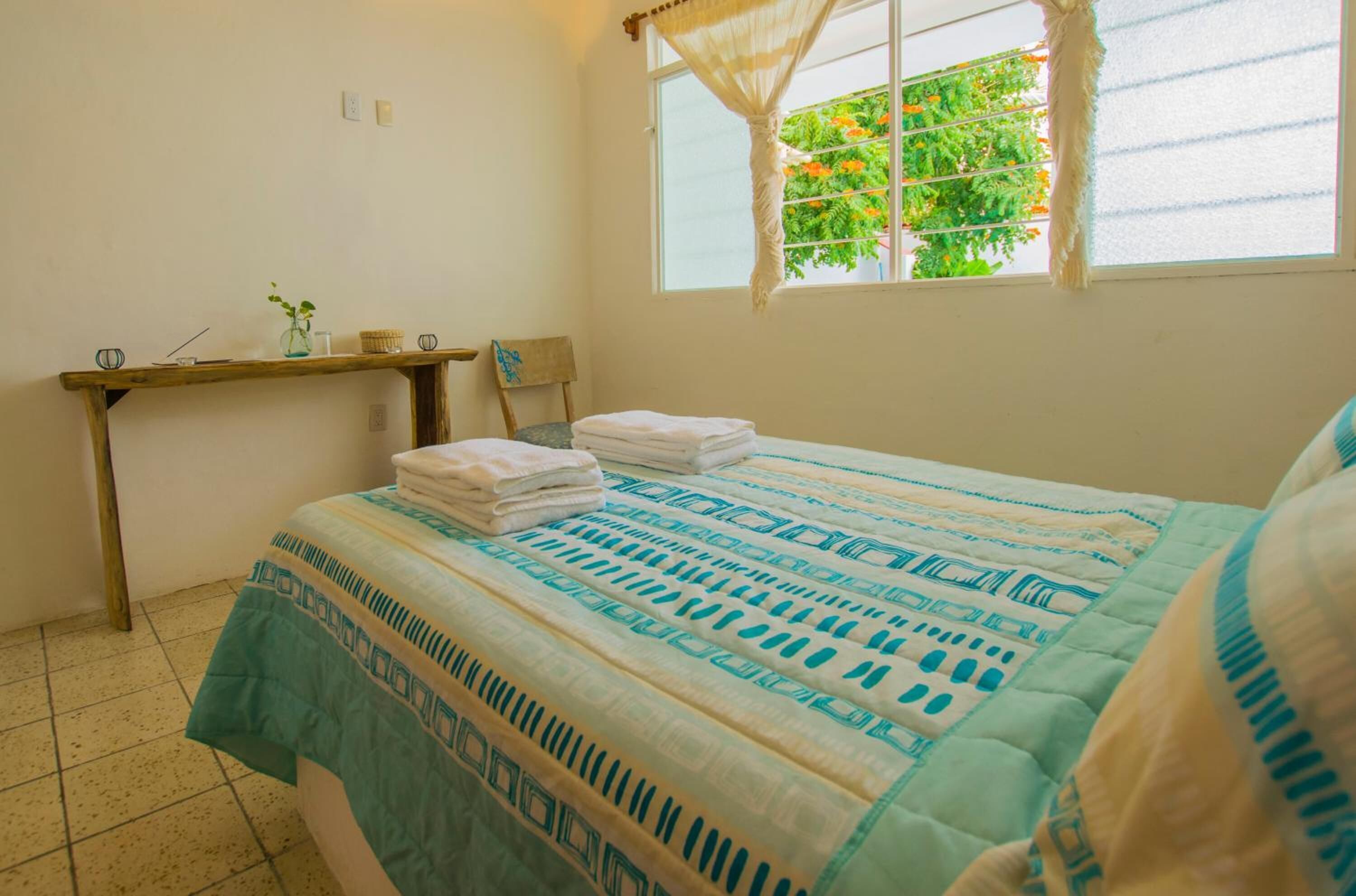 A bedroom with a bed, a bedside table, a window with curtains, and a view of greenery outside.