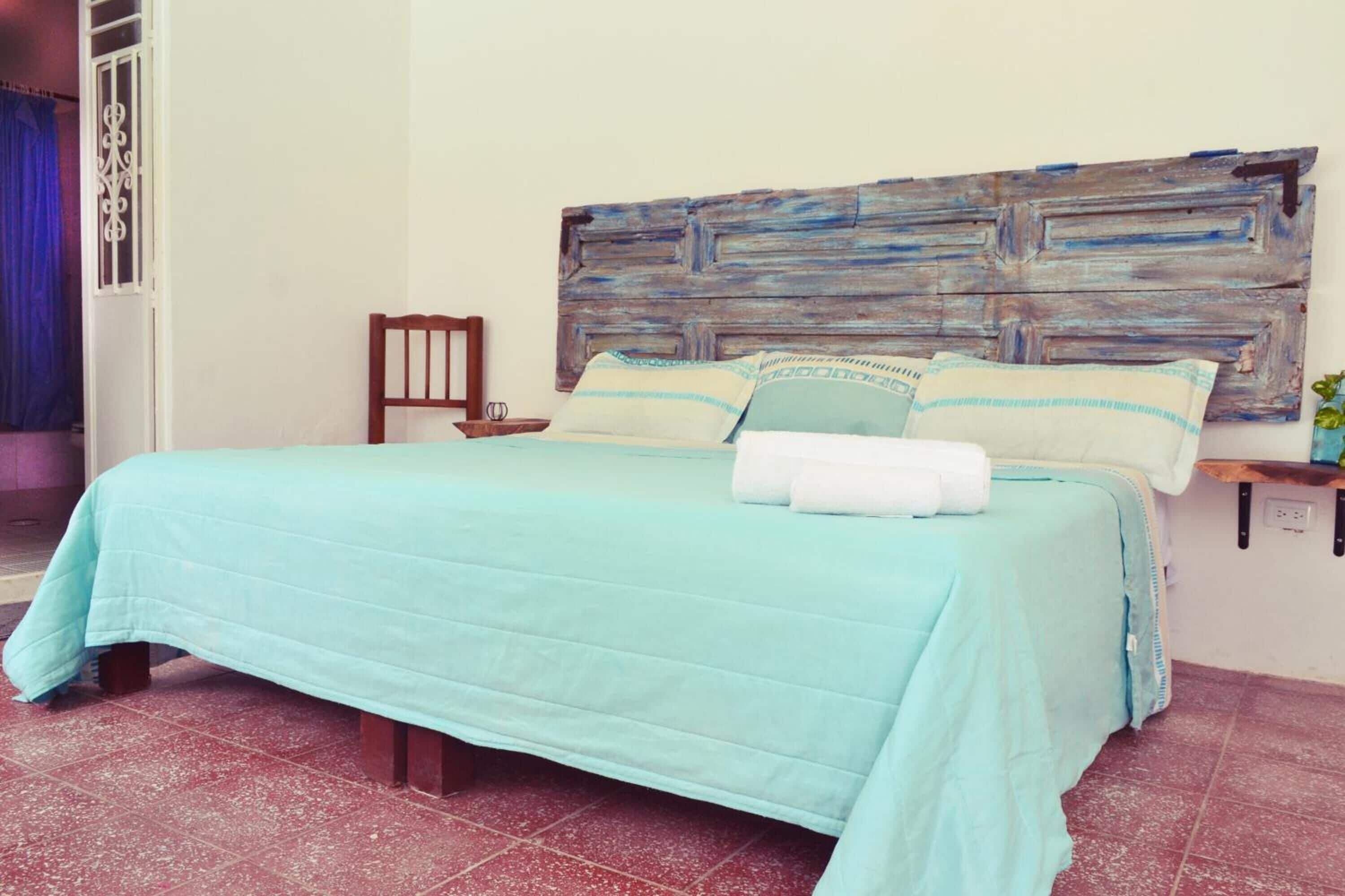Una cama con colcha y almohadas azul claro, cabecera de madera y mesita de noche con un vaso.