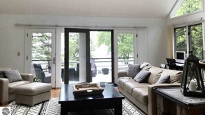 Amplia sala de estar con sofá, una mesa de centro y vistas al exterior a través de puertas correderas de vidrio.