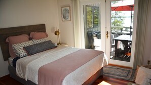 Un dormitorio con cama, mesita de noche, lámpara y vistas a un patio exterior con mesas y sillas.