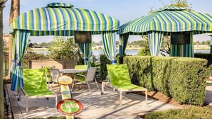 Ein Patio mit gestreiften Sonnenschirmen, grünen Stühlen, einem Tisch und einem Schild mit der Aufschrift 'CABANA 6'.