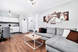 En moderne stue med en grå sofa, et træbord og et køkkenområde med hvide skabe og et køleskab.