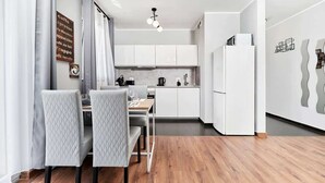 A modern kitchen with white cabinets, a dining area with two chairs, and a wooden floor.