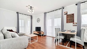A modern living room with a sofa, coffee table, TV, and dining area.