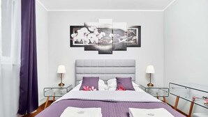 A modern hotel room with a large bed, two bedside tables, a headboard, and a wall-mounted artwork.