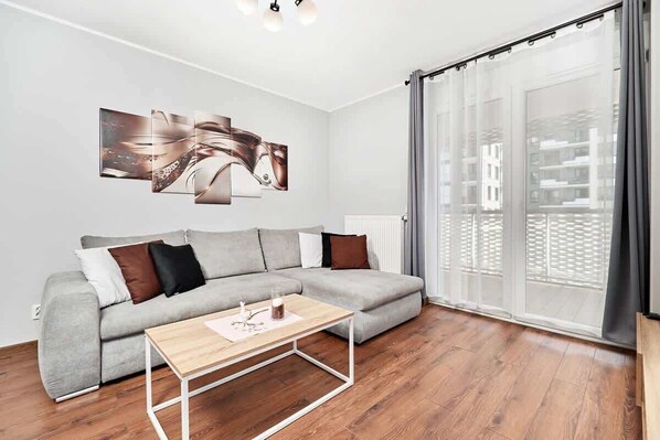 Una sala de estar moderna con un sofá seccional gris, una mesa de centro de madera y un ventanal con vistas a edificios.