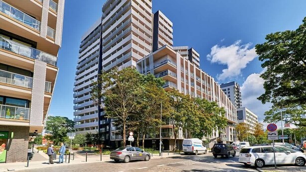 A multi-story building with balconies, a parking area, and a clear sky.
