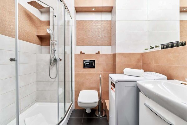 Un baño moderno con ducha de vidrio, inodoro y lavadora integrada.