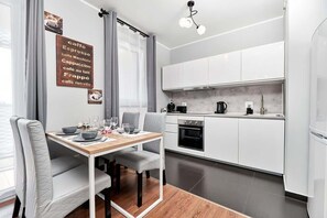Et moderne køkken med hvide skabe, et spisebord med stole og en kaffemaskine.