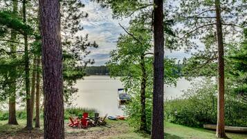 A lakeside view with trees, a dock, and a row of red Adirondack chairs.