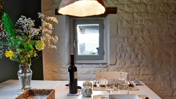 Una mesa de comedor dispuesta con una botella de vino, copas y un jarrón de flores.