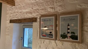 Una habitación rústica con una pared de piedra, un ventanal con vistas a árboles y dos carteles enmarcados que muestran paisajes costeros.