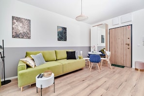Ein modernes Wohnzimmer mit einem grünen Sofa, einem Esstisch mit Stühlen, einem kleinen Beistelltisch und einem großen Spiegel.