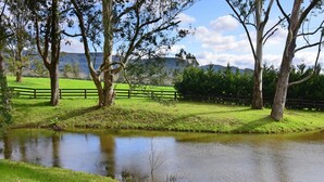 A serene landscape with a pond, trees, and a wooden fence. - Maple Cottage - Gorgeous character filled cottage (KANGAROO VALLEY)