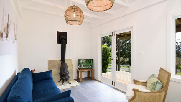 A living room with a blue sofa, a television, a fireplace, and a view of the outdoors through a glass door. - Maple Cottage - Gorgeous character filled cottage (KANGAROO VALLEY)