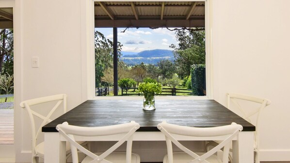 A dining area with a table and chairs, a view of a garden, and a mountain in the distance.
