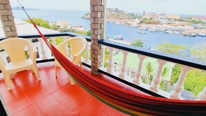 A balcony with a red floor, two white plastic chairs, and a red hammock. - Ocean View (St, George)