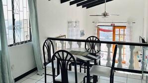 A dining area with a table and chairs, a balcony with a railing, and a view of the cityscape through the window. - Ocean View (St, George)