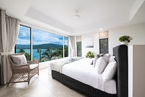 A modern hotel room with a large bed, a wicker chair, a view of the sea, and a balcony. - Splendeur Sur La Mer Two Bedroom (Airlie Beach)