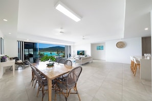 A spacious living area with a dining table, seating, and a view of the outdoors. - Splendeur Sur La Mer Two Bedroom (Airlie Beach)