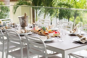 An outdoor dining area with white chairs, a table set with plates, glasses, and a bottle of champagne. - Splendeur Sur La Mer Two Bedroom (Airlie Beach)