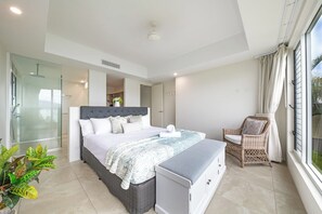 A modern bedroom with a large bed, a bedside table, a chair, and a view of the outdoors. - Splendeur Sur La Mer Two Bedroom (Airlie Beach)