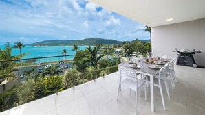 Un balcon avec une table dressée pour le dîner, offrant une vue sur la côte et un ciel dégagé.