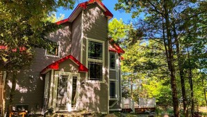 Une maison à deux étages avec un toit rouge, entourée d’arbres et de rochers.