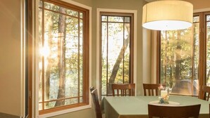 Un coin repas avec une table dressée pour quatre personnes, de grandes fenêtres donnant sur la verdure et un luminaire suspendu.